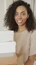 Confident woman with curly hair smiling amidst packages, symbolizing entrepreneurial success.